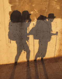 Két túrázó ember árnyéka egy útmenti falon